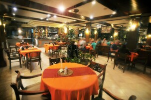 Un restaurante con varias mesas y sillas, una zona de bar y plantas en macetas.