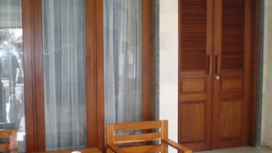 A room with a wooden table and chairs, a red mat, and two wooden doors with a decorative stone design above them. - Swastika Guest House (Denpasar)