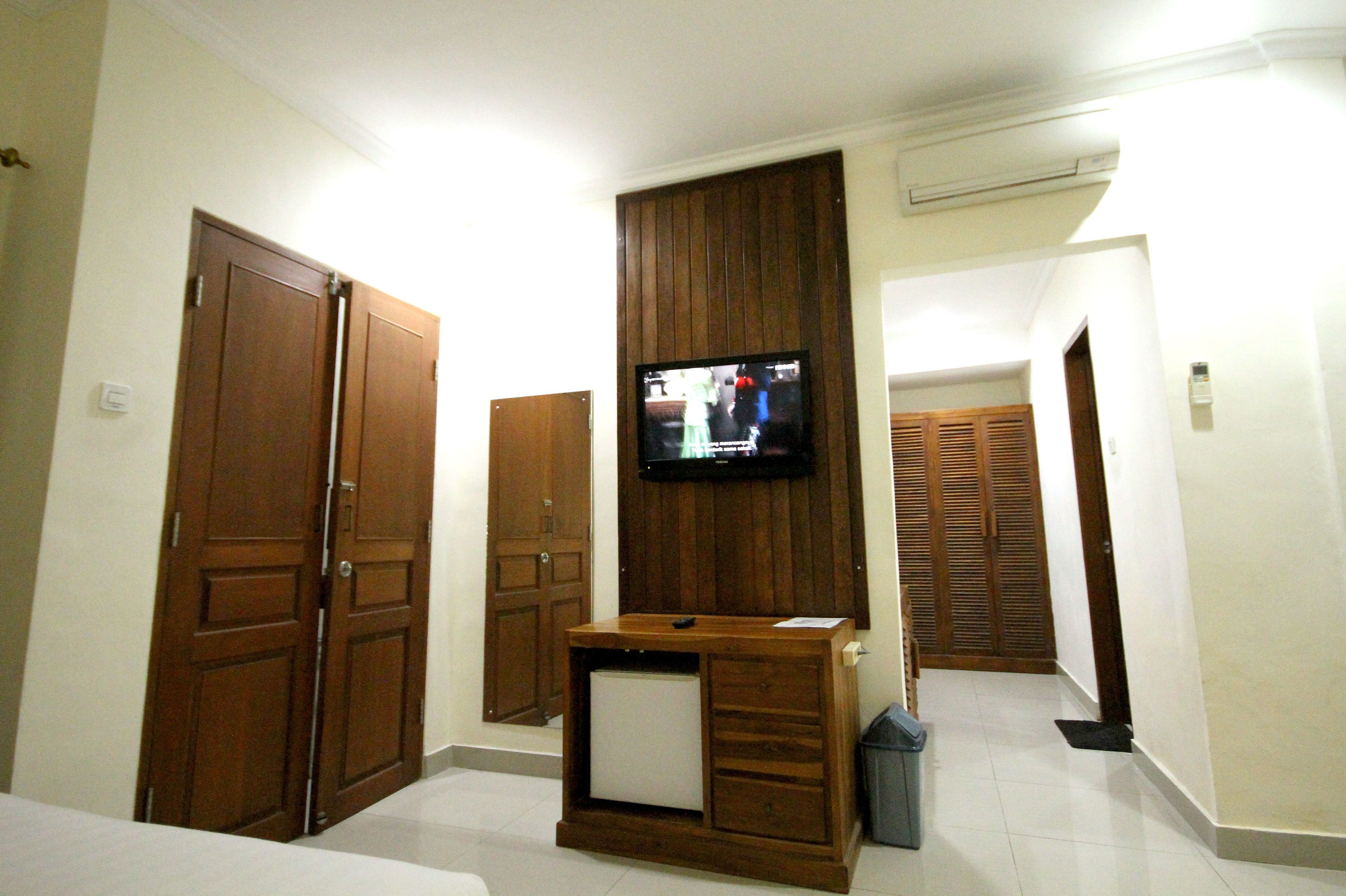 Habitación de hotel con un televisor montado en un mueble de madera, una mesita y dos armarios.