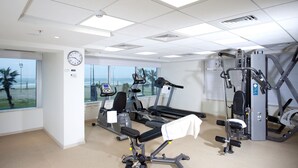 A gym with exercise equipment, a clock, and a window with a view of the ocean.