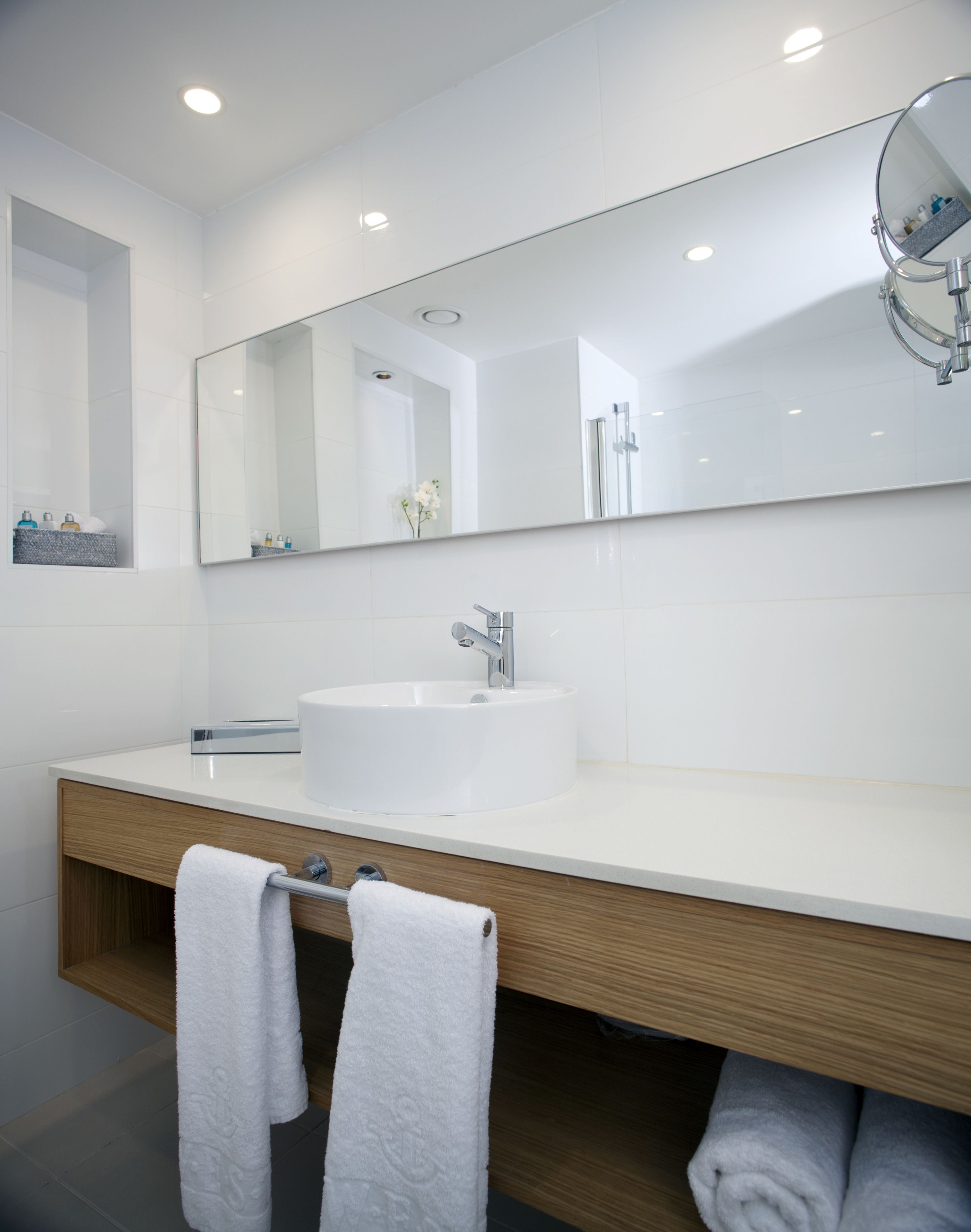 A modern bathroom with a white sink, a large mirror, and two towels hanging on a towel rack.