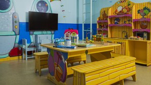 A playroom with a table, chairs, a bench, a television, and a wall with space-themed decorations.