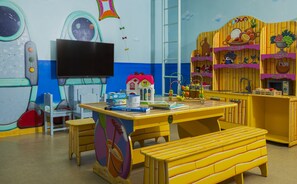 A playroom with a table, chairs, a bench, a television, and a wall with space-themed decorations. - Brown Seaside Ashdod (Ashdod)