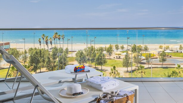 A balcony with a view of the beach, a table with a hat and a basket, and a toy car. - West All Suite Boutique Ashdod (Ashdod)