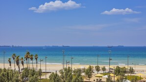 A beach with palm trees, umbrellas, and a view of the ocean with ships in the distance. - West All Suite Boutique Ashdod (Ashdod)