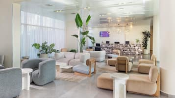 A modern hotel lobby with a reception desk, seating area, and large windows.
