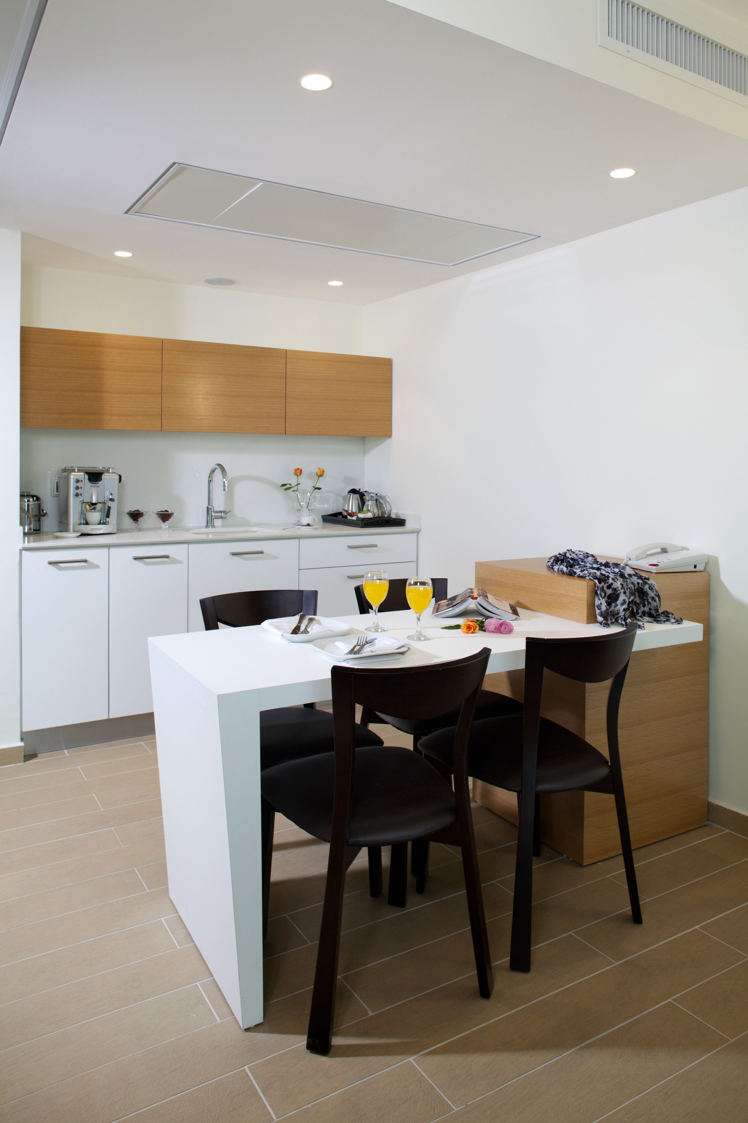 Uma cozinha compacta com armários brancos, uma máquina de café e um espaço de refeições com duas cadeiras e uma mesa.