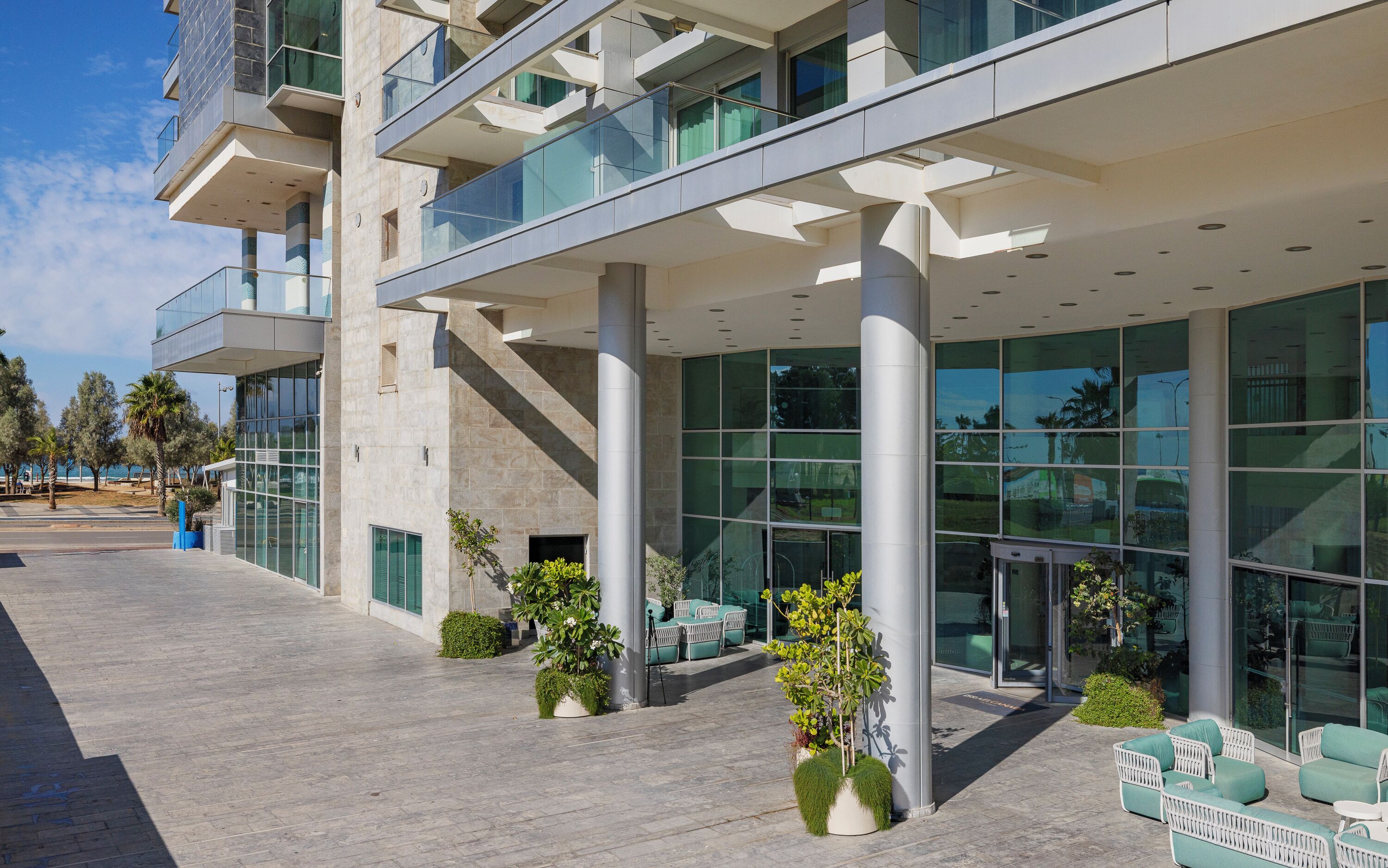 A modern building with a glass facade, outdoor seating, and a clear sky.