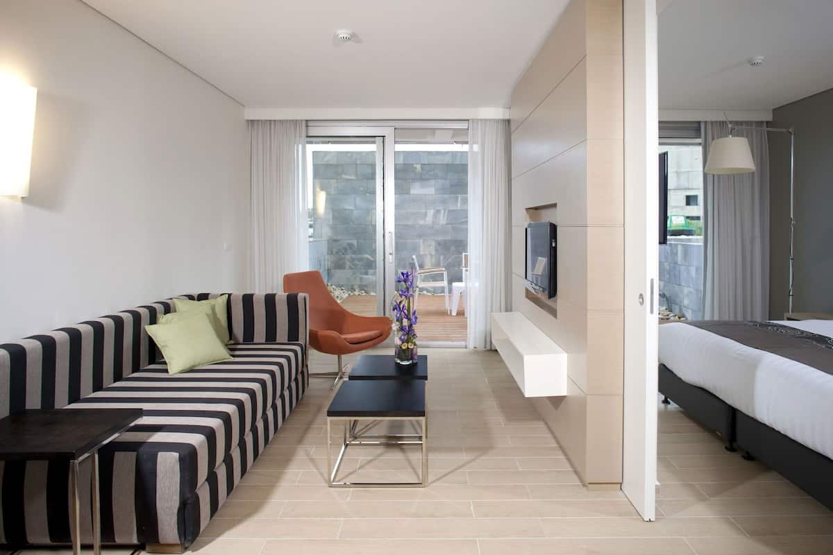 A modern hotel room with a striped sofa, a small table, a TV mounted on the wall, and a bed.
