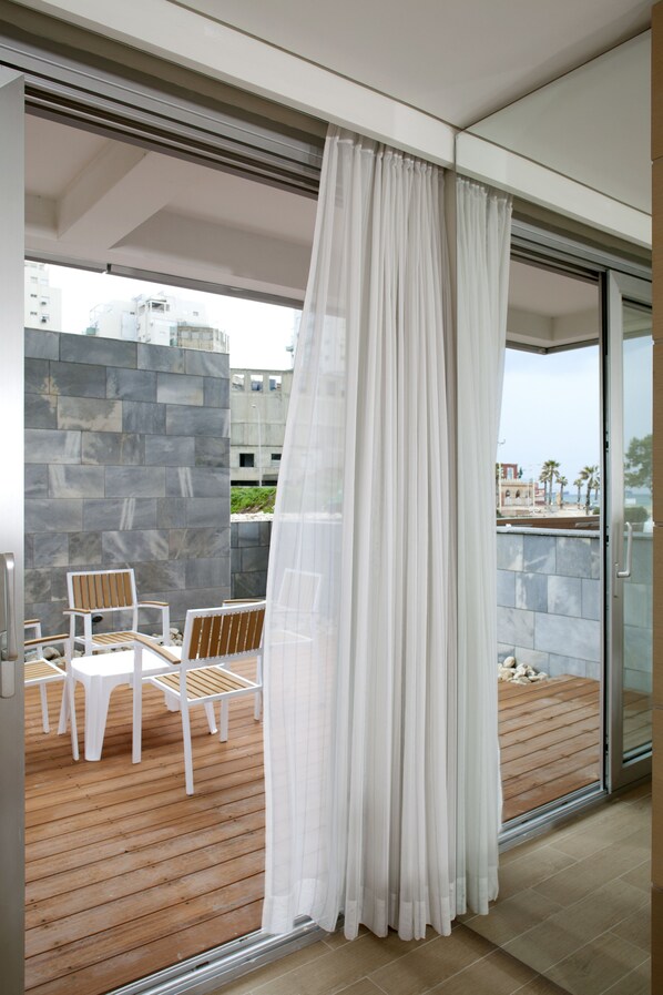 A balcony with a white curtain, a wooden deck, and a white chair. - Brown Seaside Ashdod (Ashdod)
