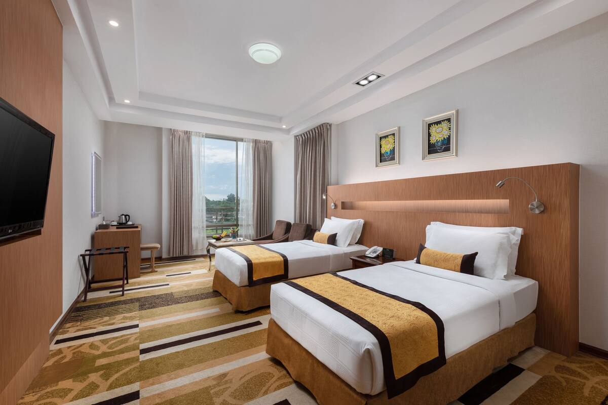 A hotel room with two beds, a desk, a television, and a large window with curtains.