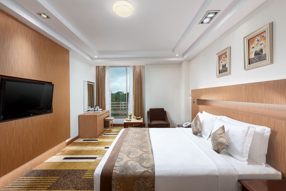A hotel room with a large bed, a flat-screen TV, a desk, and a chair.