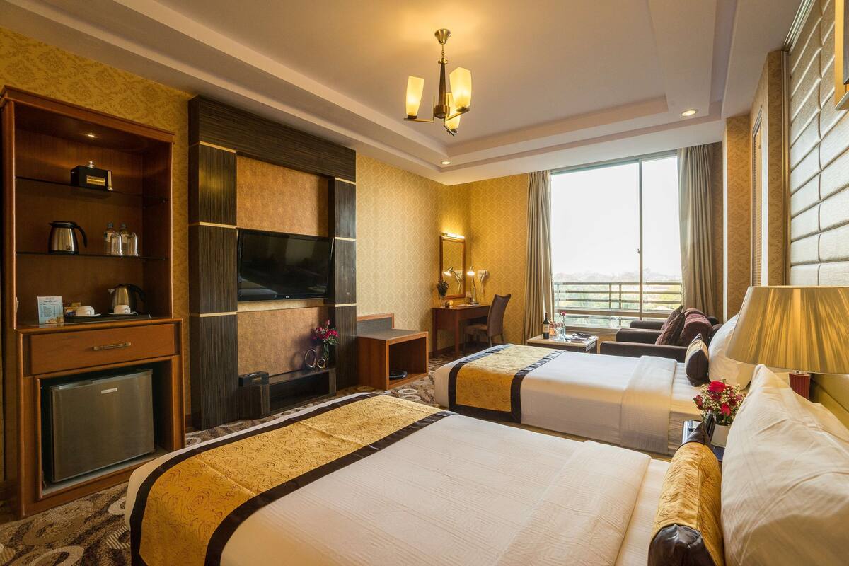 A hotel room with two beds, a television, a desk, and a view of the city.