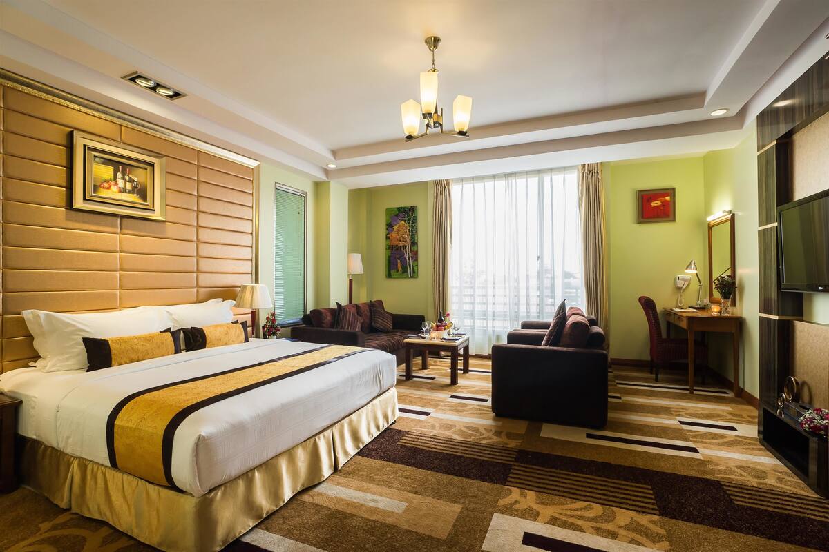 A hotel room with a large bed, a sofa, a desk, and a television.