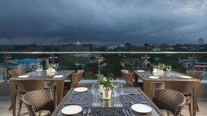 A rooftop restaurant with tables set for dining, wicker chairs, and a view of a cityscape and a temple in the distance. - Best Western Green Hill Hotel (Yangon)