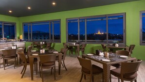 A dining area with multiple tables and chairs, large windows with city views, and a green wall. - Best Western Green Hill Hotel (Yangon)