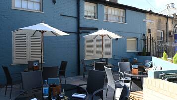 An outdoor patio with tables and chairs, two umbrellas, and a brick wall.