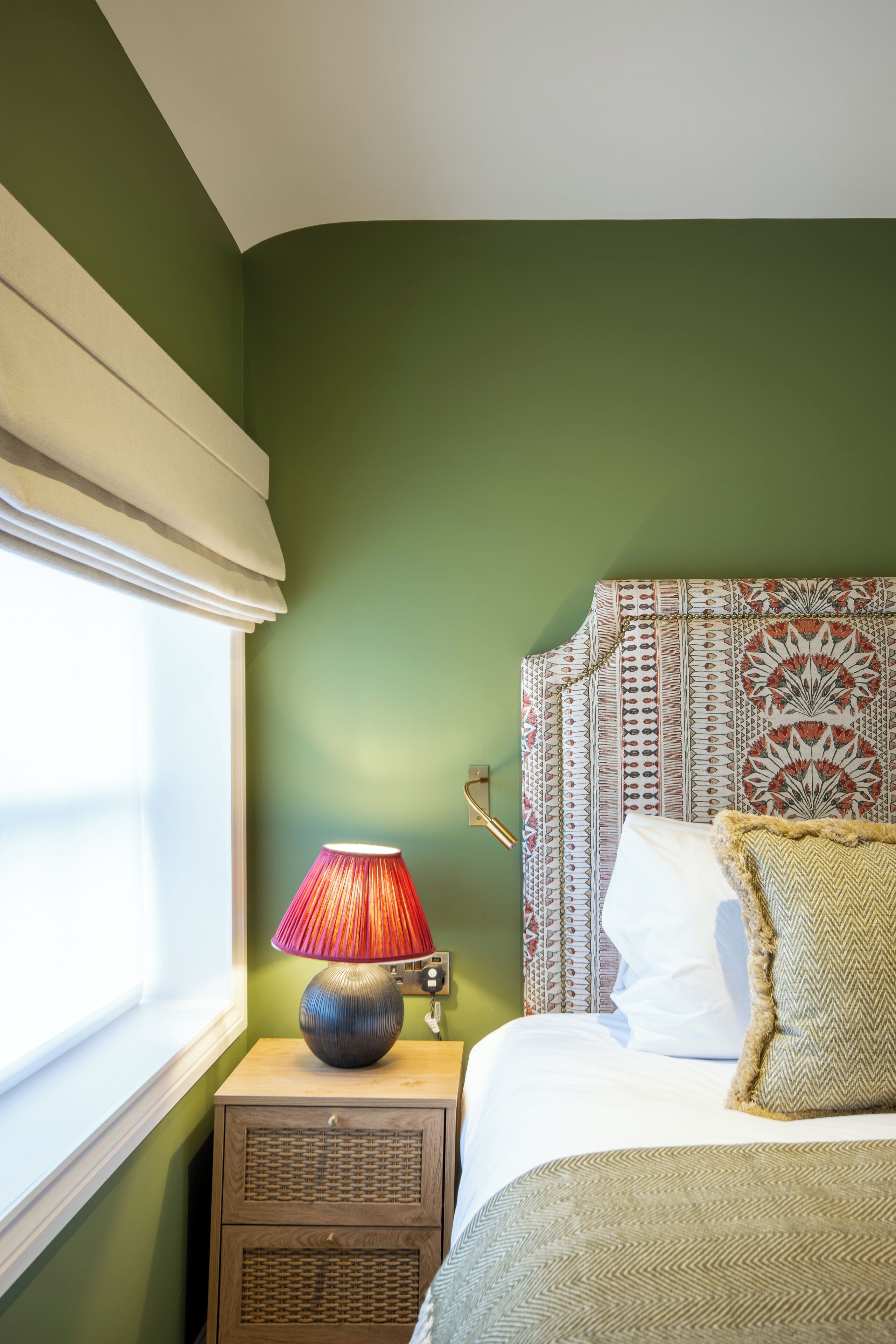 A neatly made bed with patterned bedding, a bedside lamp, and a nightstand with drawers.