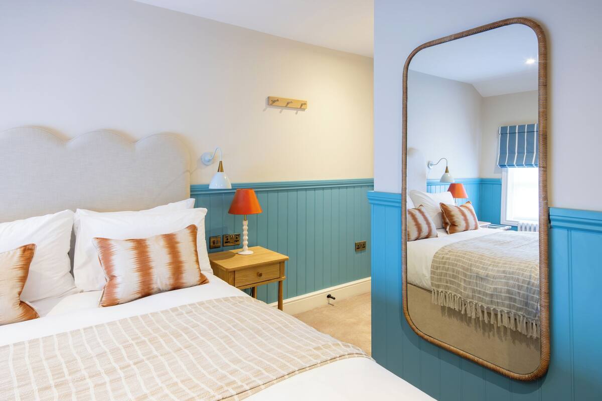 A bedroom with a bed, bedside table, lamp, and a mirror.