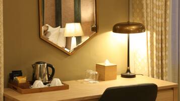 A hotel room desk with a lamp, a tissue box, a coffee pot, and a chair.