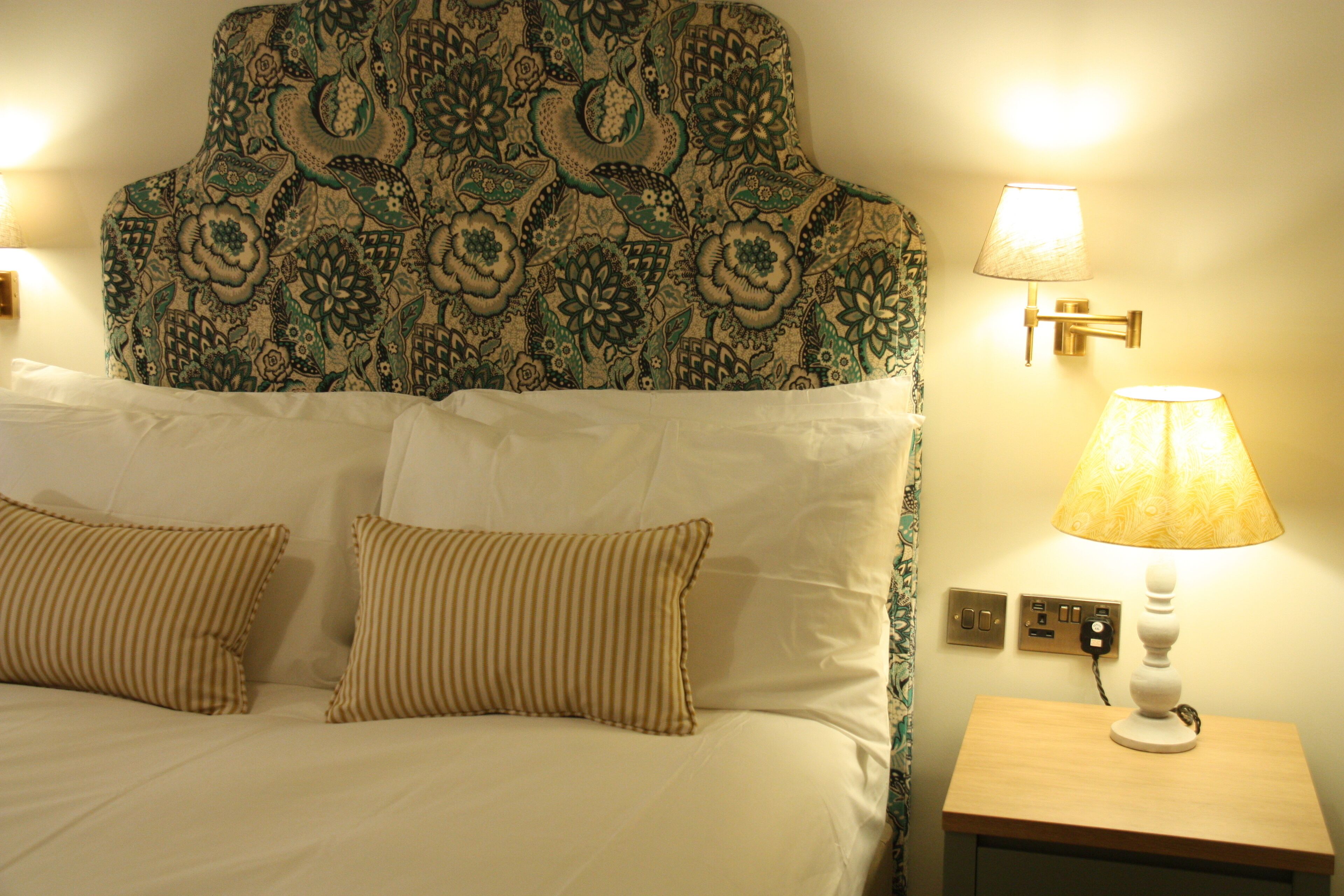 A hotel room with a bed, two pillows, a patterned headboard, and two wall-mounted lamps.