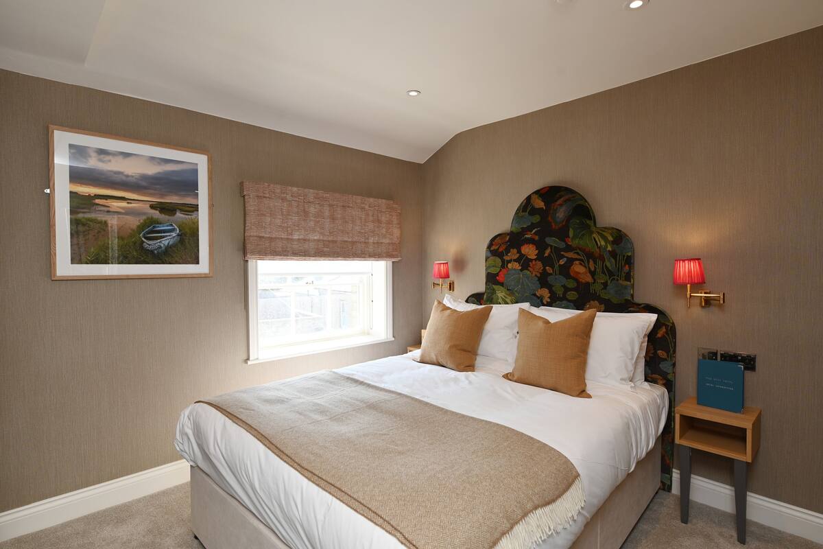 A neatly made bed with a headboard, a bedside table with a lamp, and a framed picture on the wall.