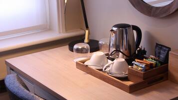 A wooden desk with a black lamp, a coffee pot, and a tray with cups and a coffee maker.