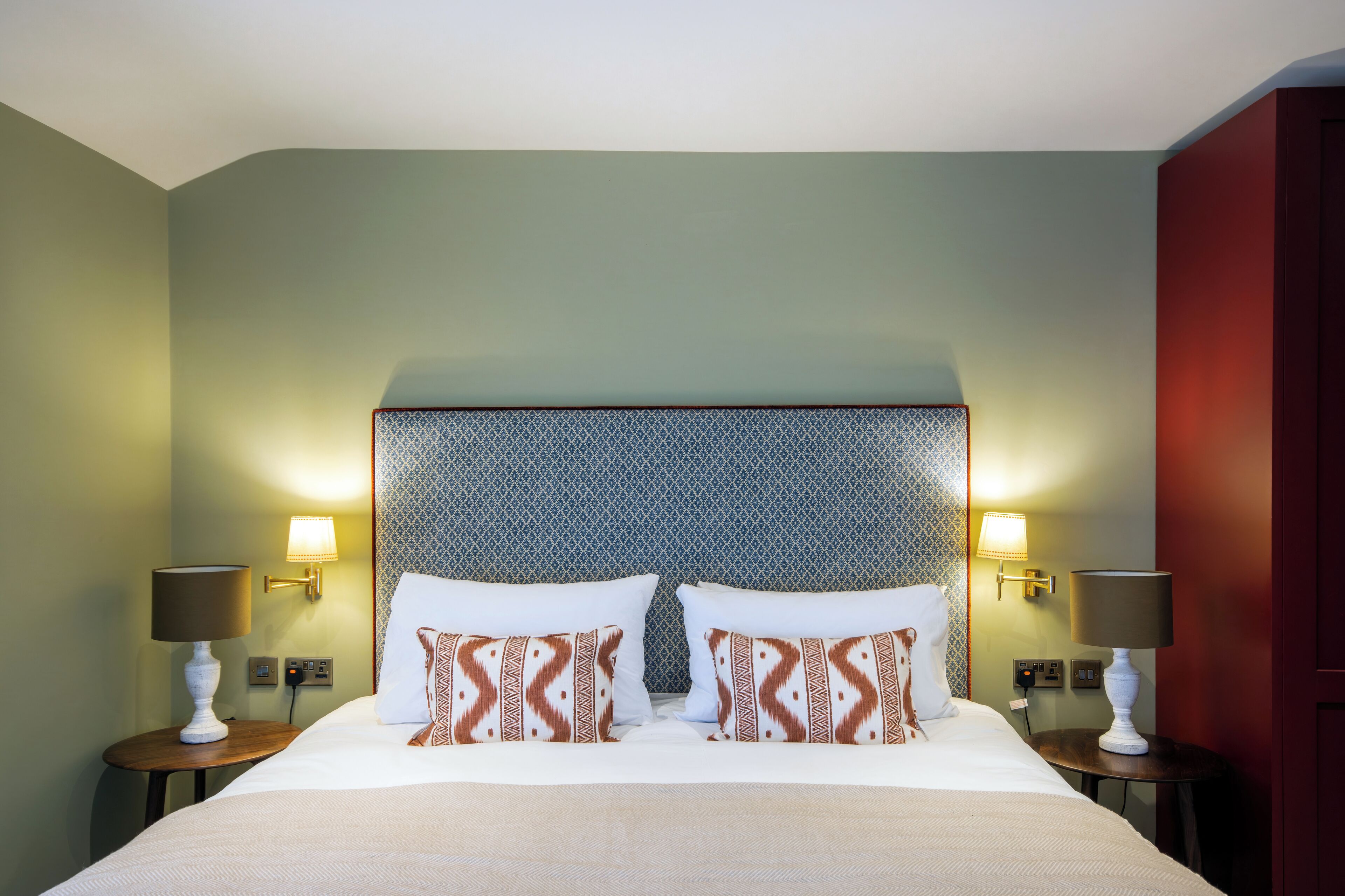 A hotel room with a large bed, two bedside tables with lamps, patterned pillows, and a textured headboard.