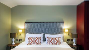 Una habitación de hotel con una cama grande, dos mesitas de noche con lámparas, almohadas estampadas y un cabecero con textura.
