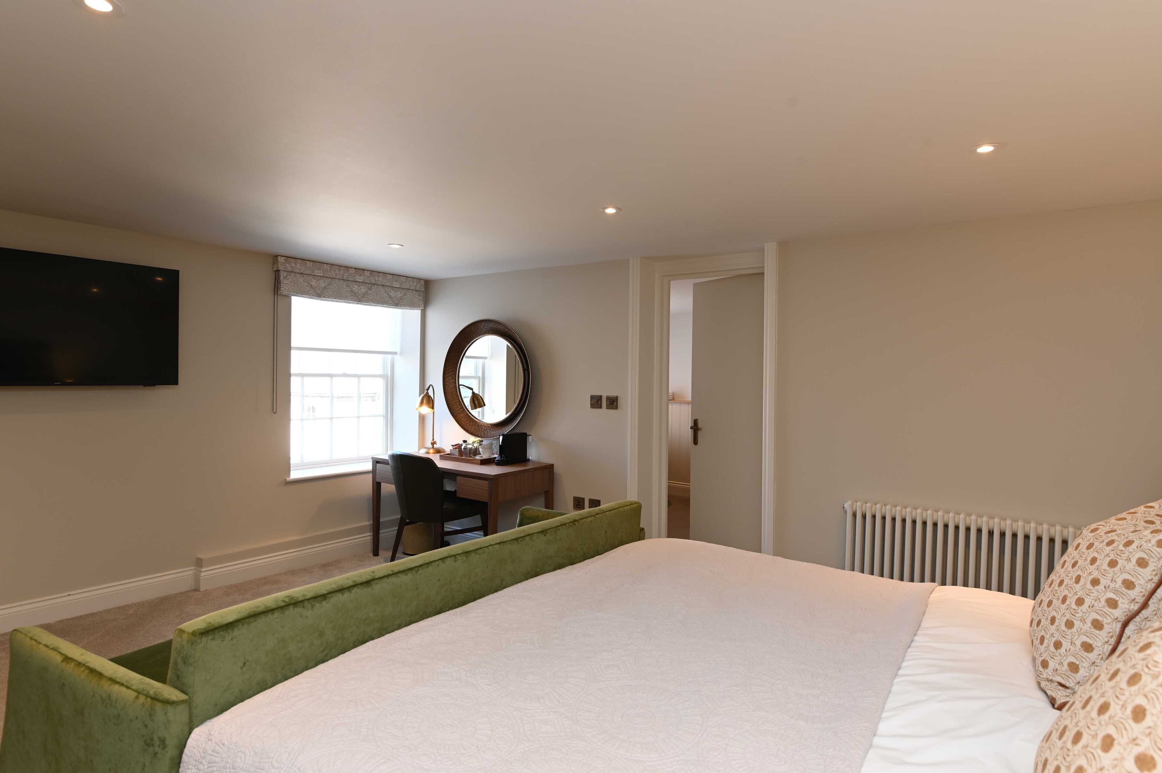 A bedroom with a large bed, a desk with a chair, a mirror, and a television mounted on the wall.