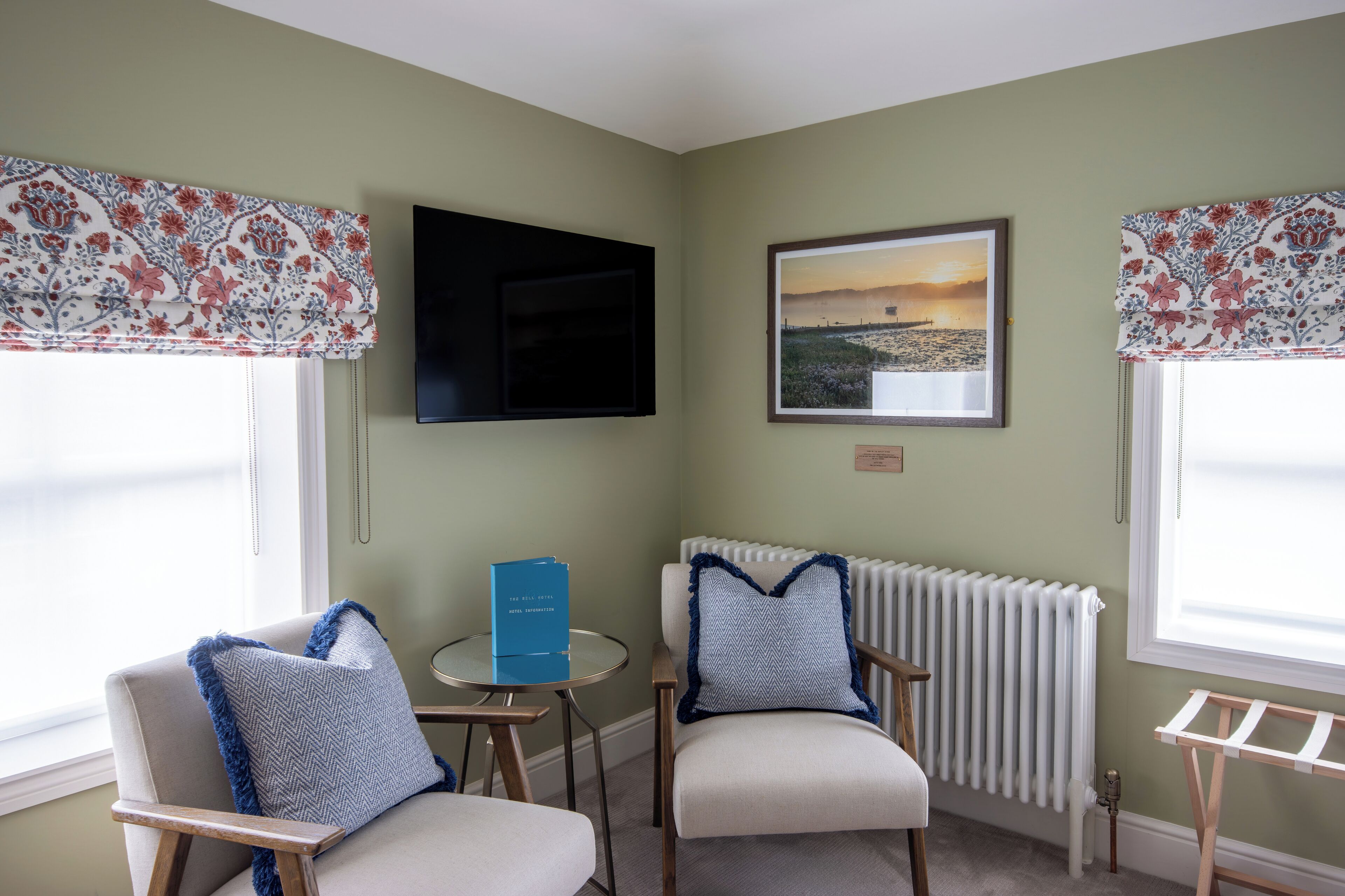 A corner room with two chairs, a small table, a radiator, and a framed picture on the wall.