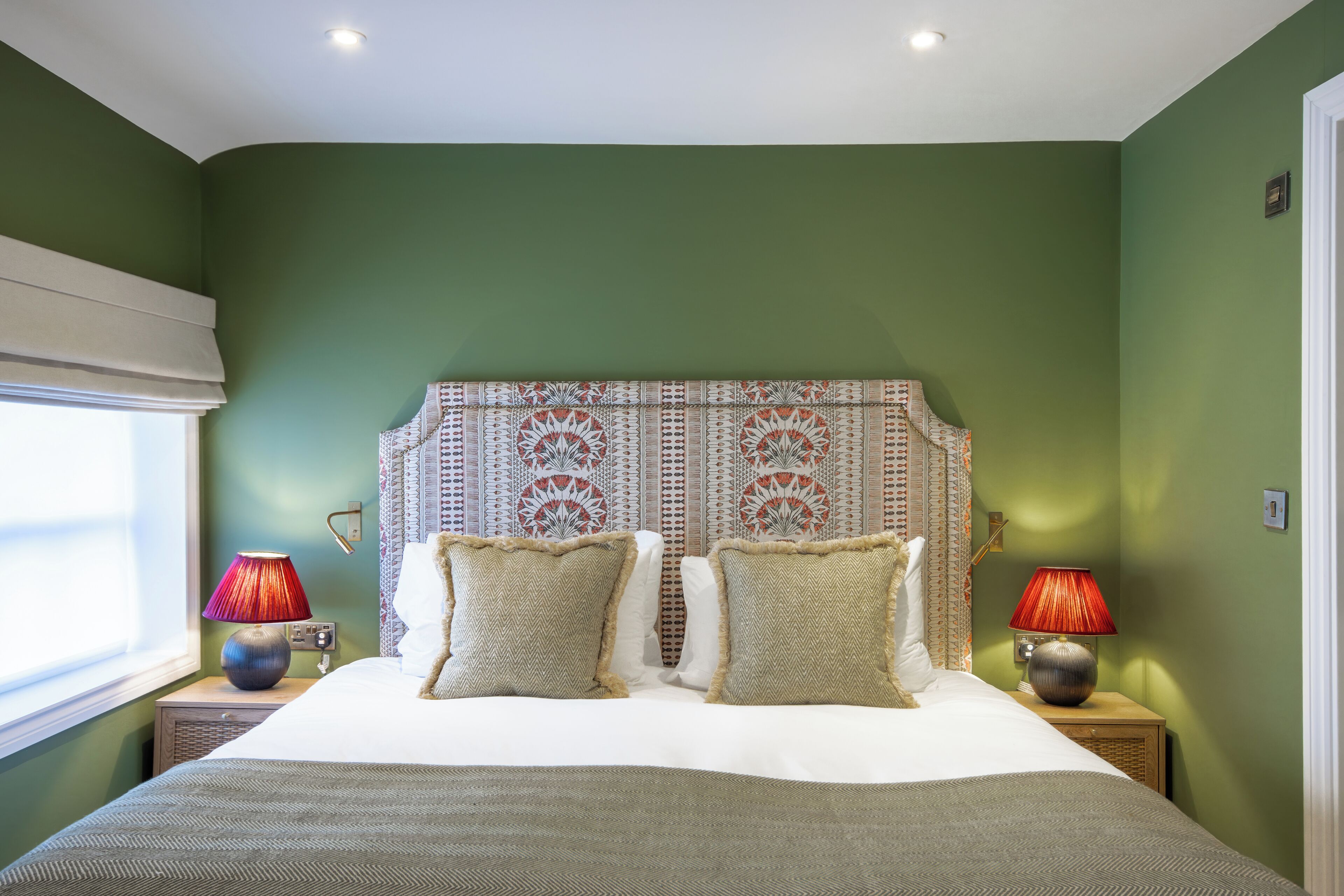 A bedroom with a large bed, two nightstands with lamps, a patterned headboard, and green walls.