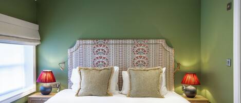 A bedroom with a large bed, two nightstands with lamps, a patterned headboard, and green walls.