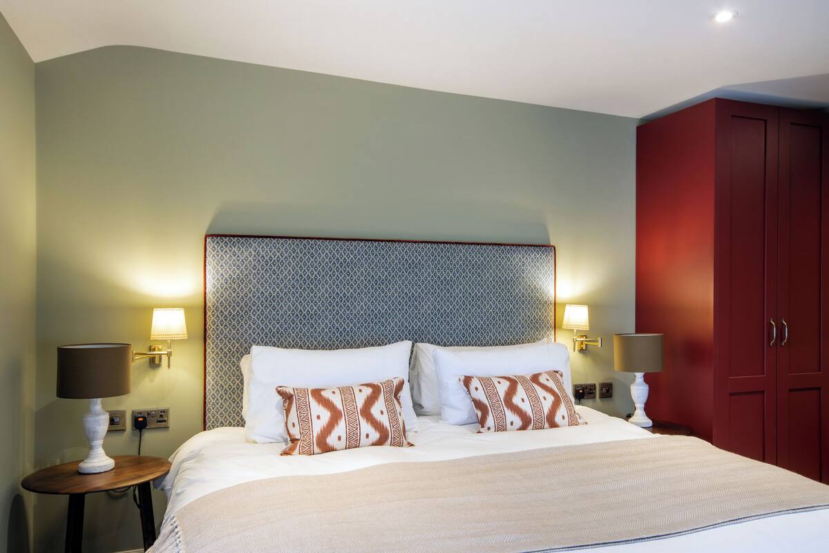 A neatly made bed with patterned pillows, a headboard with a geometric design, and two bedside lamps.