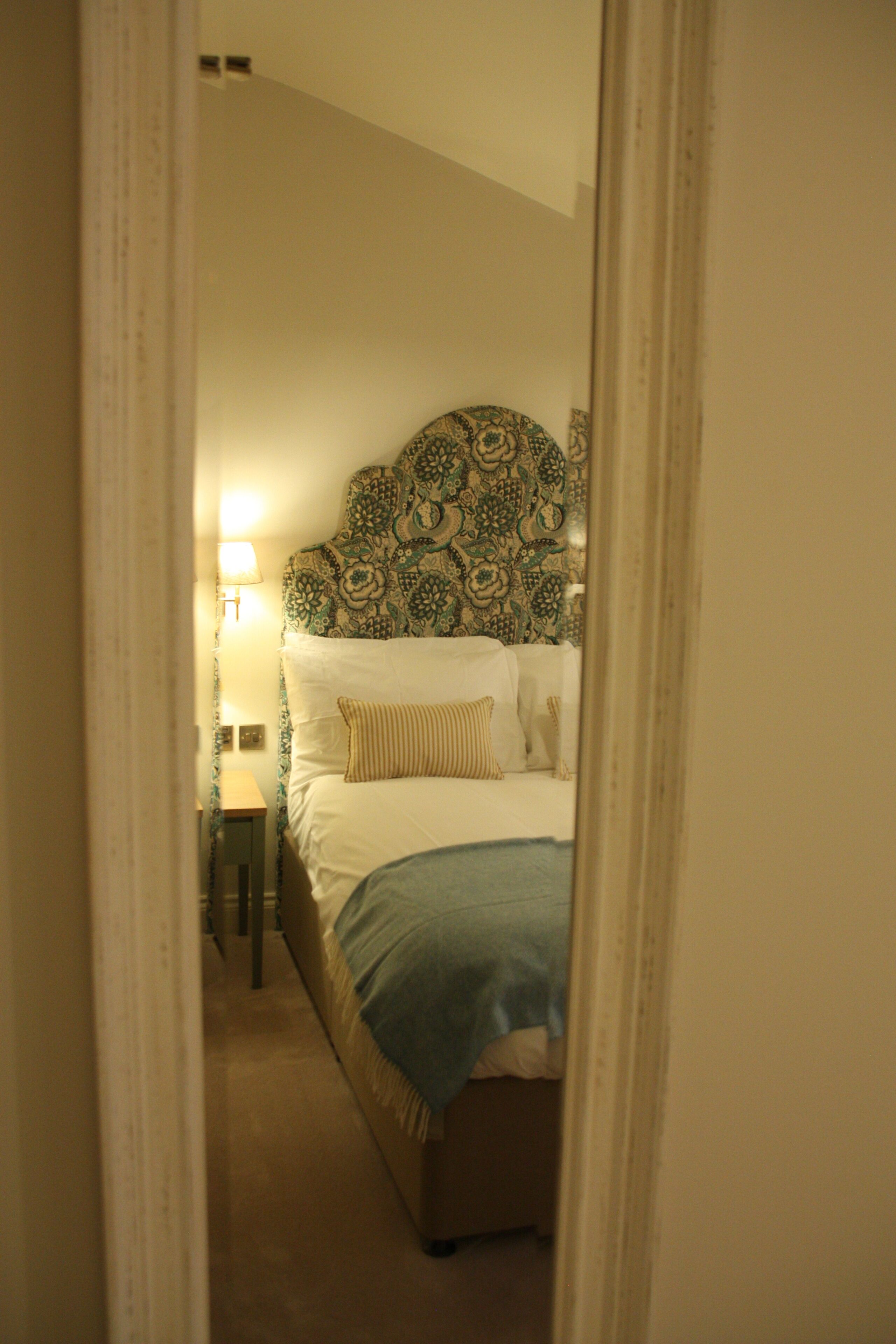 A bedroom with a patterned headboard, a bedside lamp, and a bed with a blue blanket.