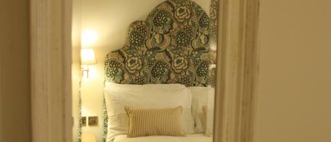 A bedroom with a patterned headboard, a bedside lamp, and a bed with a blue blanket.