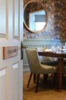 Uma porta com a inscrição "COACH ROOM", com uma mesa de jantar e cadeiras ao fundo.