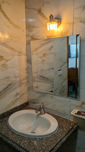 Un baño con pared de mármol, un lavamanos con encimera de granito y un espejo con lámpara colgante.