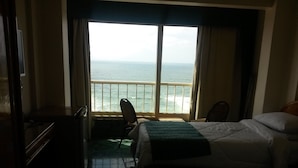 A hotel room with two beds, a chair, a desk, and a view of the ocean through large windows. - Royal Crown Hotel (Alexandria)