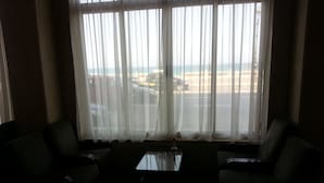 A room with two dark-colored sofas facing a window with sheer white curtains. A small table is in the center. - Royal Crown Hotel (Alexandria)