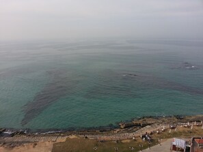 Zona costera con un espigón rocoso y un paseo marítimo con mesas y sombrillas.