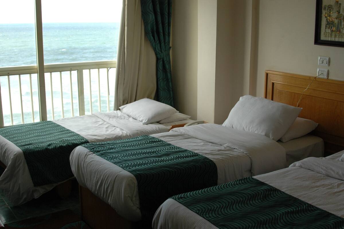 A hotel room with two beds, a view of the sea, and a wooden headboard.