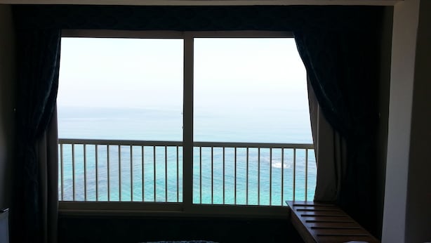 A room with a large window overlooking the sea, a bed with a patterned bedspread, and a wooden bench. - Royal Crown Hotel (Alexandria)