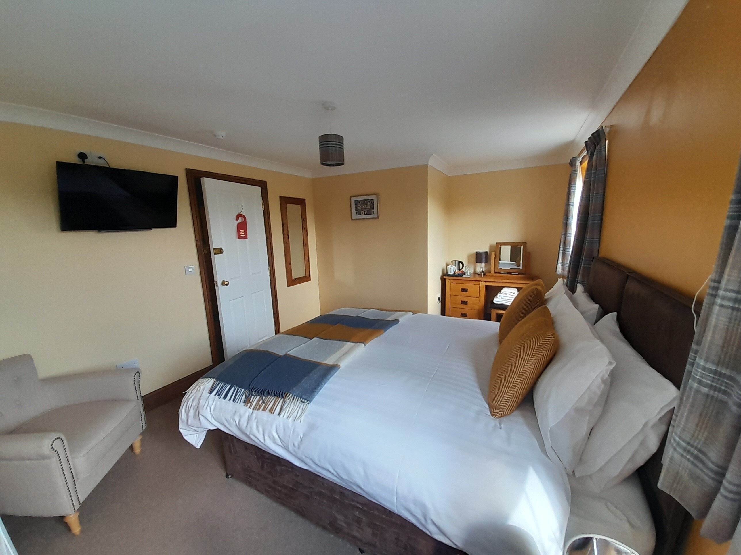 Habitación de hotel con cama, escritorio, silla, televisión y ventana con cortinas.