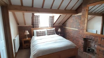 A bedroom with a wooden ceiling, a brick wall, a bed with pillows, two bedside tables with lamps, and a window with curtains.