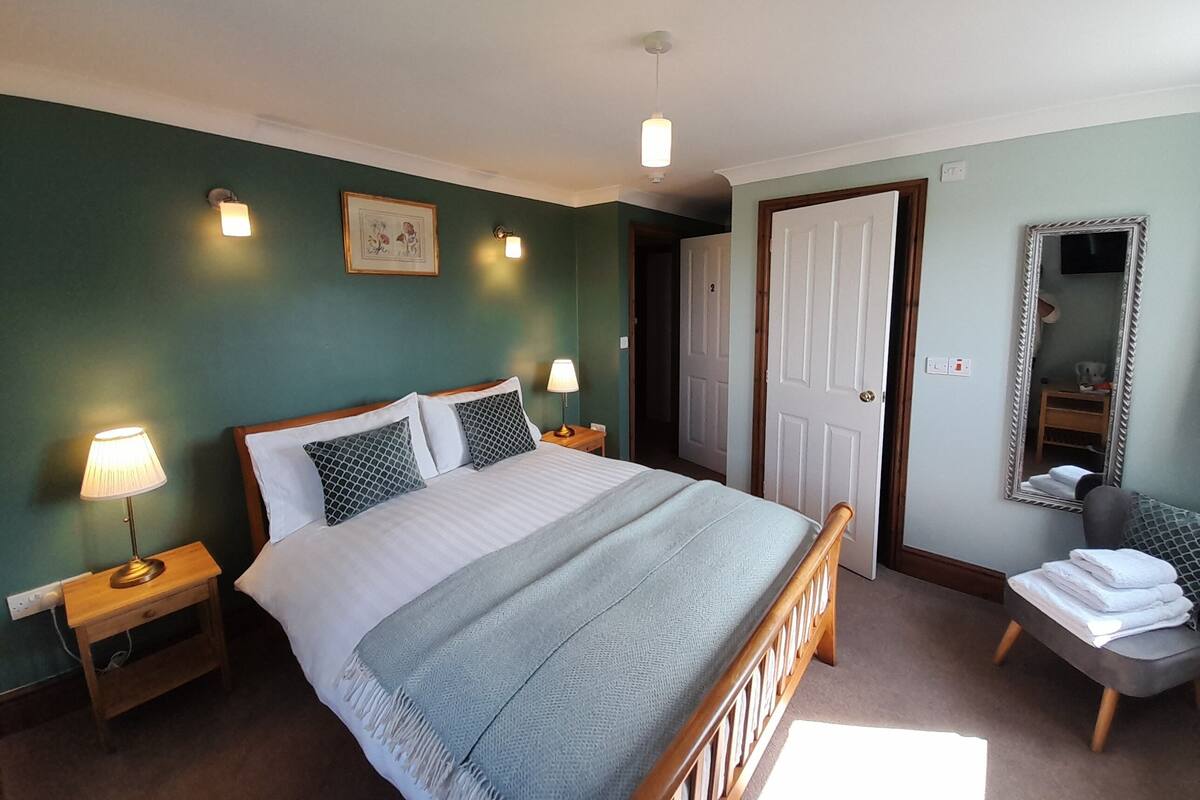 Ein Schlafzimmer mit Bett, Nachttischlampen, einem Spiegel und einer Tür.