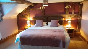 A bedroom with a large bed, wooden beams, two bedside lamps, and a sloped ceiling.