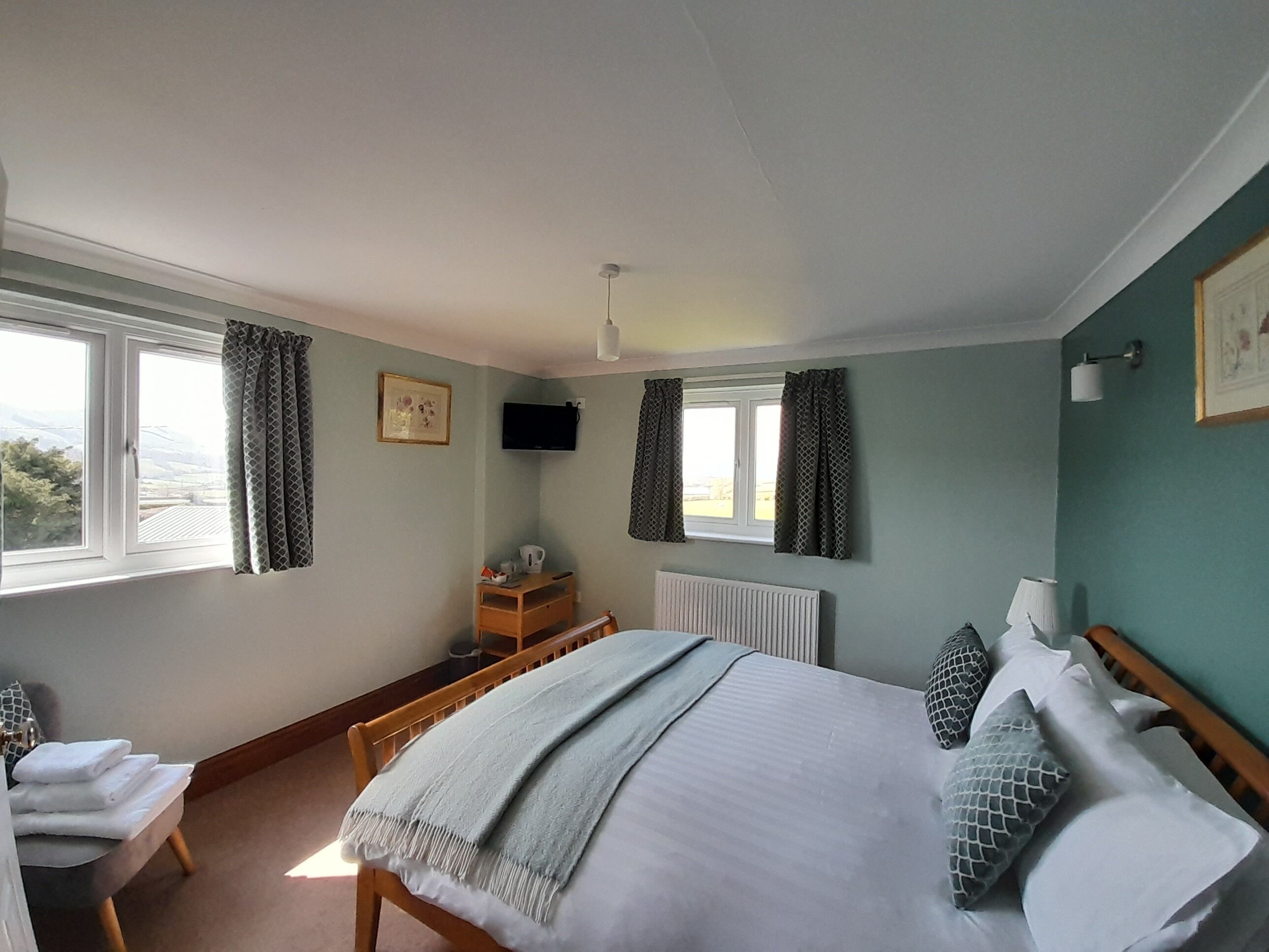 Een slaapkamer met een bed, een stoel, een bureau, een televisie en een raam met gordijnen.