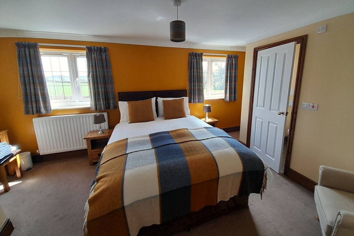 Ein Schlafzimmer mit einem großen Bett, zwei Nachttischen, einer Heizung, einem Fenster mit Vorhängen und einer Tür.