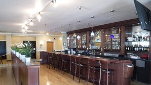 A bar area with wooden flooring, multiple bar stools, and a bar counter. There are shelves with bottles and glasses, and a television mounted on the wall. - Wingate by Wyndham Mount Vernon (Mount Vernon)